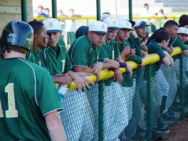 Damien players stand along the dugout rail rooting on their teammates.