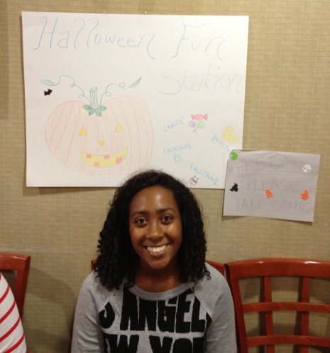 Alexis sits in front of the sign she created to invite kids to the impromptu Halloween party.